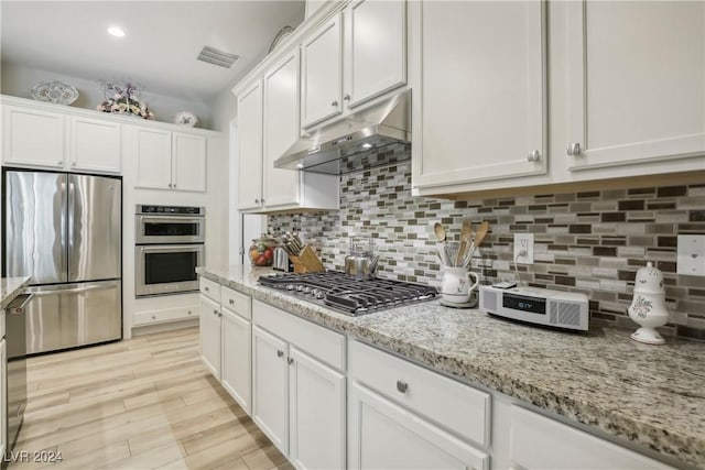 kitchen with stainless steel appliances, tasteful backsplash, light stone countertops, and white cabinets