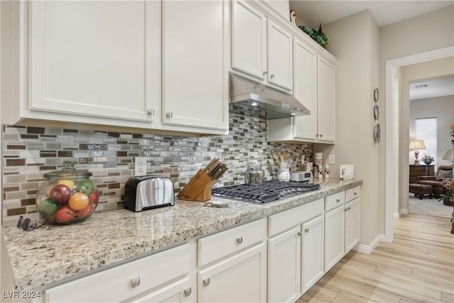 kitchen featuring light stone counters, stainless steel gas stovetop, light hardwood / wood-style floors, and white cabinets