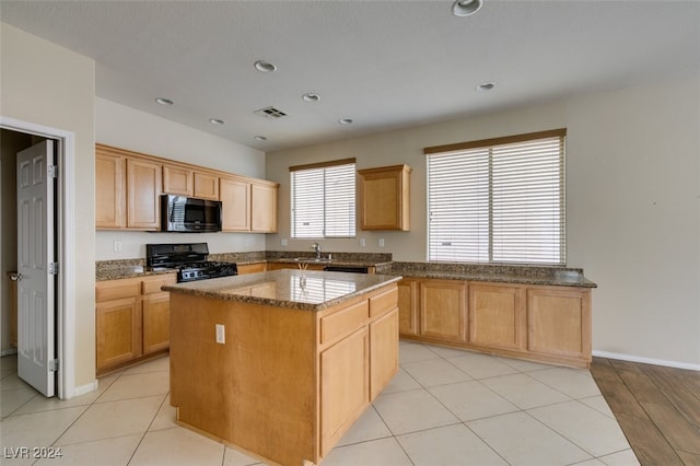 kitchen featuring dark stone countertops, a center island, light hardwood / wood-style flooring, sink, and black appliances