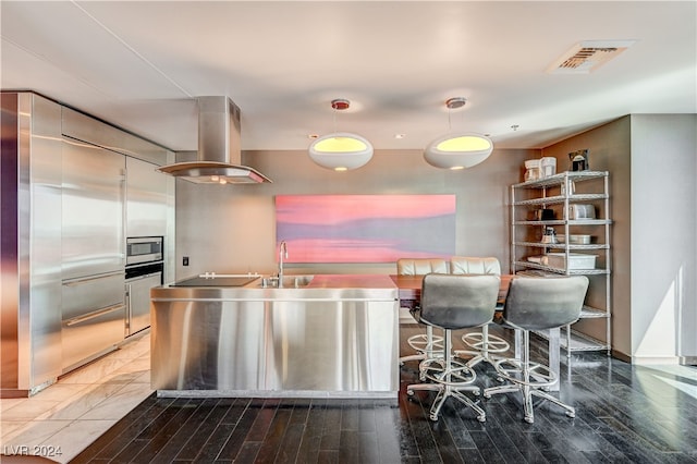 kitchen with island range hood, wood finished floors, visible vents, stainless steel microwave, and decorative light fixtures