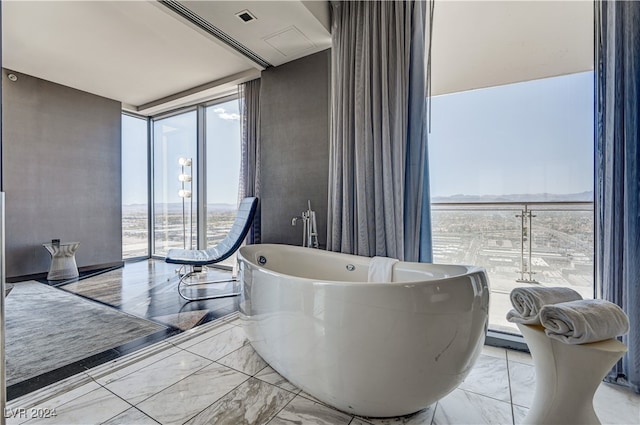 bathroom with marble finish floor, a baseboard heating unit, a wall of windows, and a freestanding bath