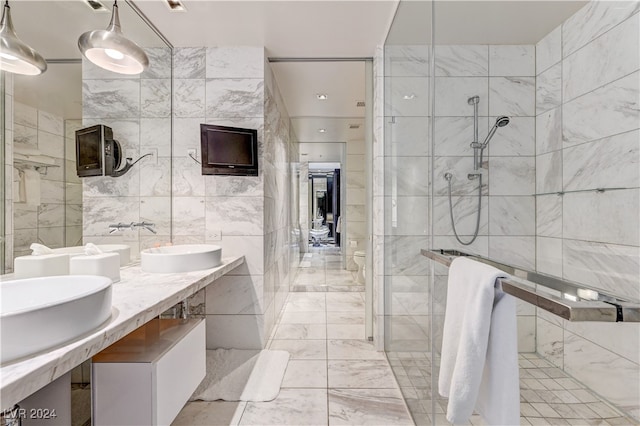 full bathroom with double vanity, tile walls, marble finish floor, walk in shower, and a sink