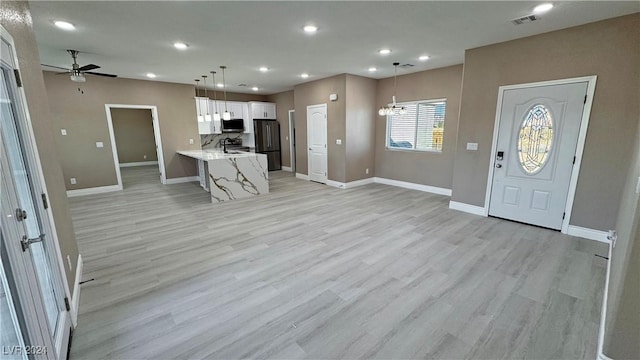 interior space with pendant lighting, ceiling fan with notable chandelier, kitchen peninsula, light hardwood / wood-style floors, and white cabinetry