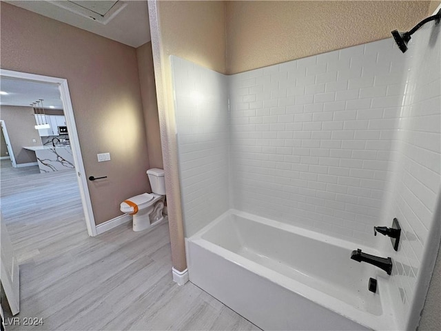 bathroom with hardwood / wood-style flooring, toilet, and tiled shower / bath