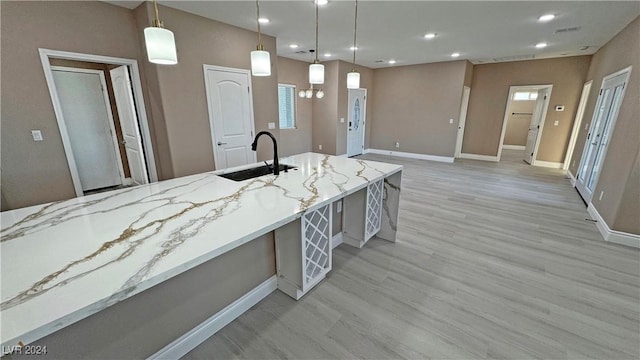 kitchen featuring pendant lighting, light hardwood / wood-style floors, light stone counters, and sink