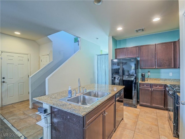 kitchen with a kitchen island with sink, black appliances, sink, light stone countertops, and light tile patterned floors