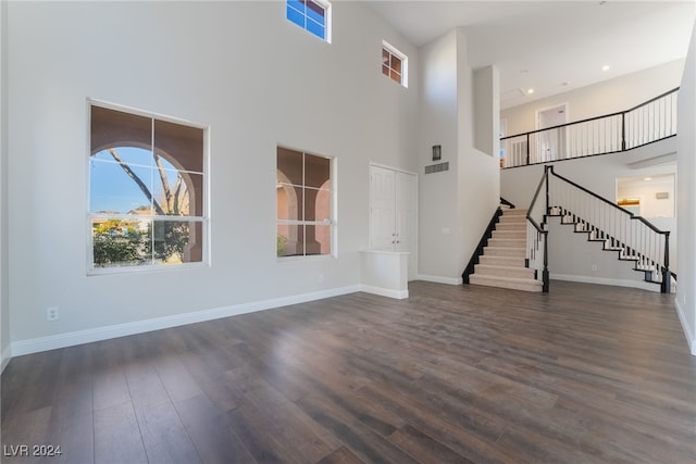 unfurnished living room featuring a towering ceiling and dark hardwood / wood-style floors