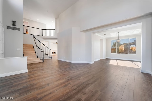 unfurnished living room with ceiling fan, dark wood-type flooring, and a towering ceiling