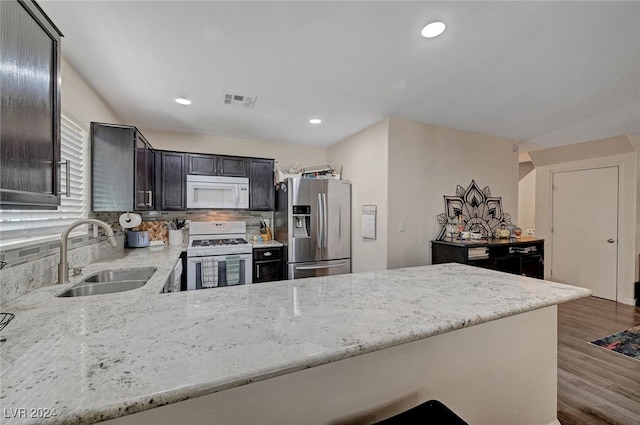 kitchen with dark hardwood / wood-style floors, light stone countertops, white appliances, tasteful backsplash, and sink