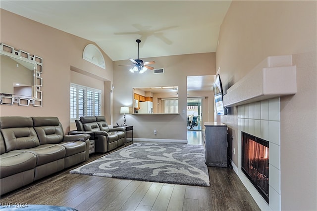 living room featuring vaulted ceiling, ceiling fan, a tile fireplace, and dark wood-type flooring