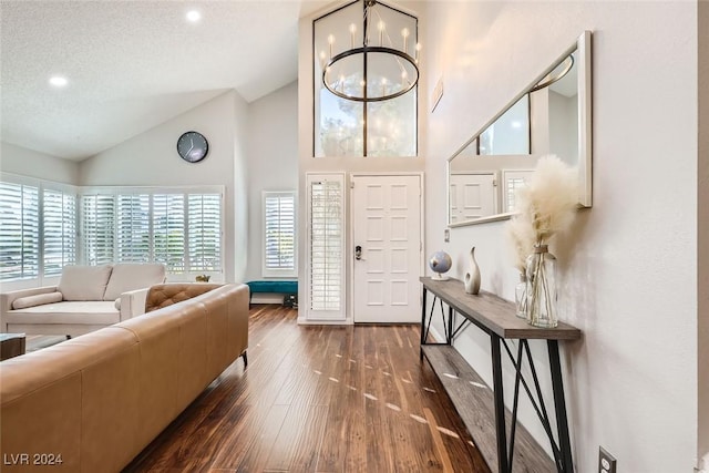 foyer entrance featuring high vaulted ceiling, a notable chandelier, dark wood-style flooring, and a textured ceiling