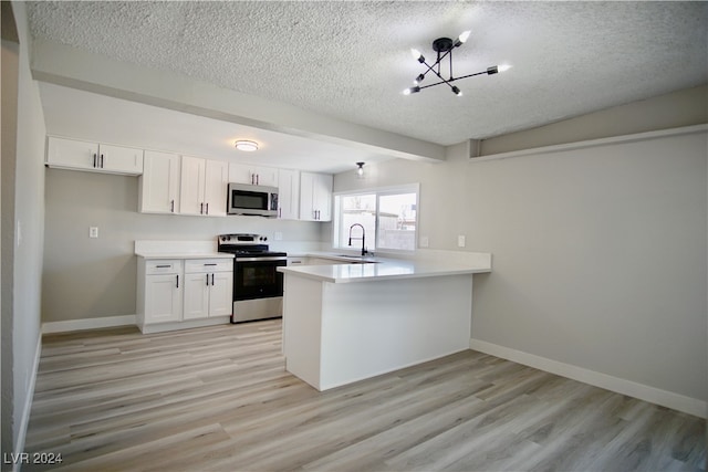 kitchen with a textured ceiling, kitchen peninsula, appliances with stainless steel finishes, white cabinets, and light hardwood / wood-style floors