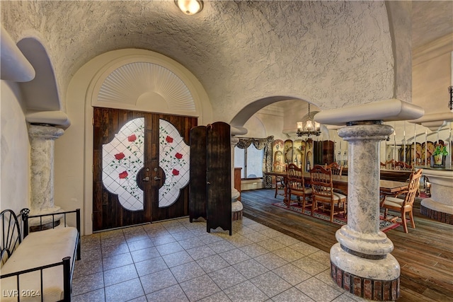 foyer with an inviting chandelier, french doors, ornate columns, hardwood / wood-style flooring, and lofted ceiling