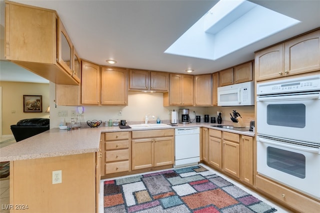 kitchen with a skylight, light brown cabinetry, white appliances, sink, and kitchen peninsula