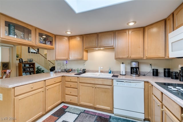 kitchen featuring white appliances, light brown cabinetry, kitchen peninsula, sink, and a skylight