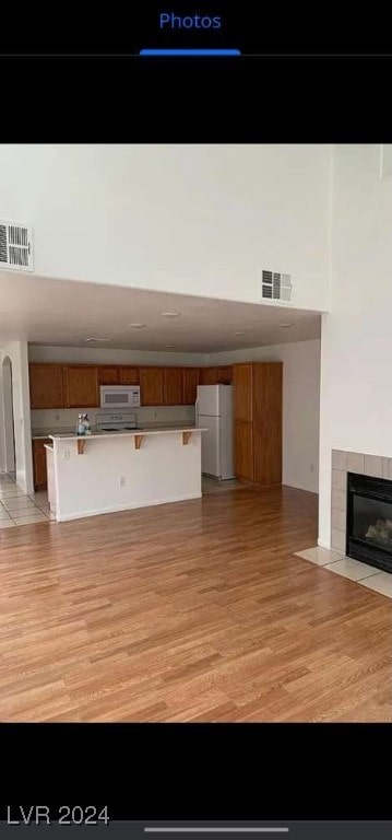 unfurnished living room featuring a towering ceiling, light hardwood / wood-style floors, and a tile fireplace