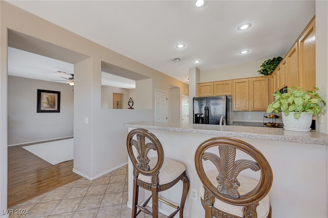 kitchen featuring kitchen peninsula, light wood-type flooring, black fridge, a breakfast bar, and light brown cabinets