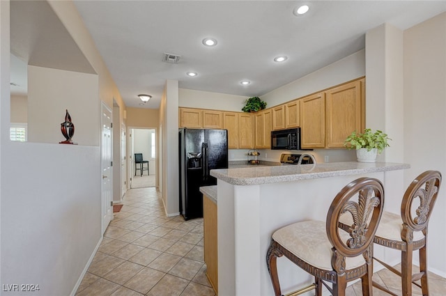 kitchen featuring kitchen peninsula, a breakfast bar, black appliances, and light brown cabinets