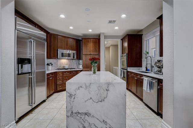 kitchen with stainless steel appliances, decorative backsplash, sink, light tile patterned floors, and a kitchen island