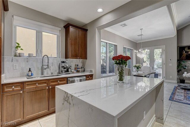 kitchen featuring decorative backsplash, a notable chandelier, sink, a kitchen island, and light stone countertops