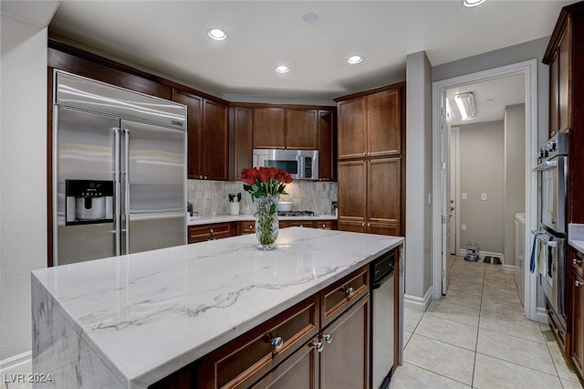 kitchen featuring tasteful backsplash, light stone counters, stainless steel appliances, light tile patterned floors, and a center island