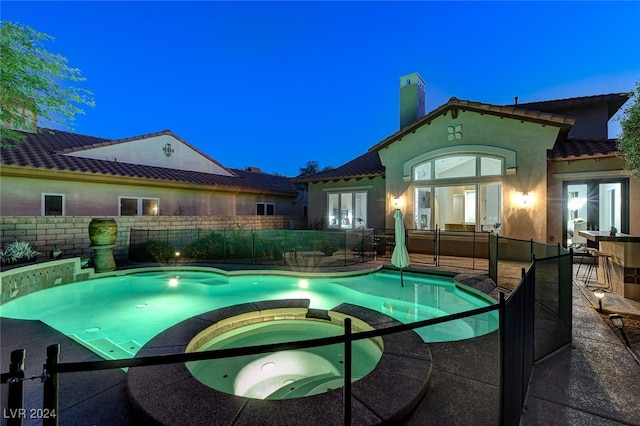 pool at dusk with an in ground hot tub and a patio area