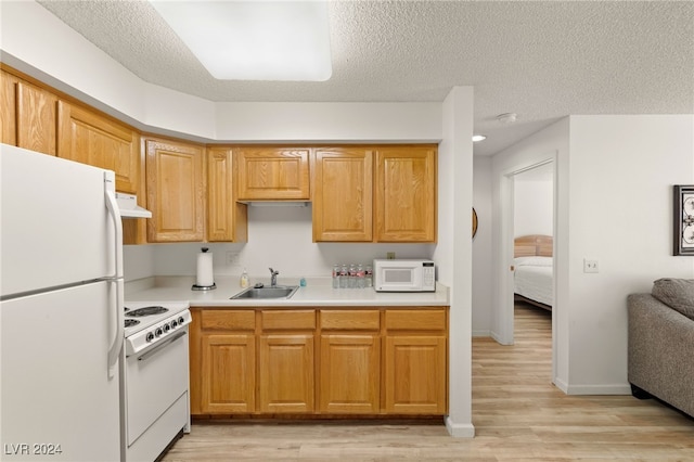 kitchen with light wood-type flooring, white appliances, sink, and a textured ceiling