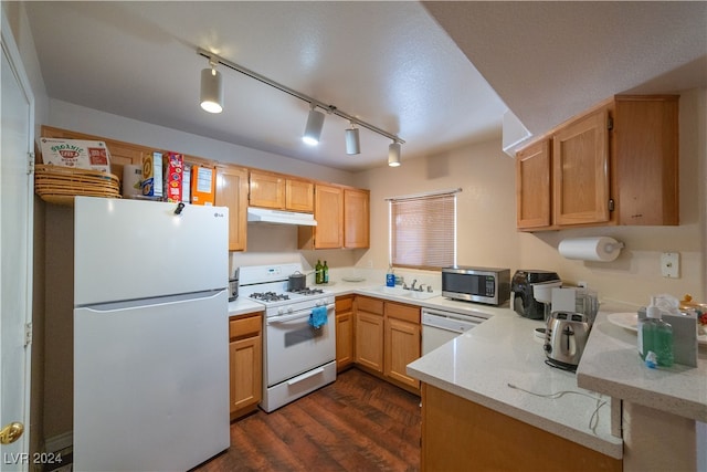 kitchen featuring track lighting, white appliances, light stone counters, sink, and dark wood-type flooring