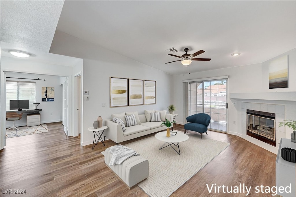 living room featuring hardwood / wood-style floors, vaulted ceiling, a tile fireplace, and ceiling fan