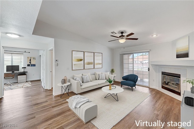 living room featuring hardwood / wood-style floors, vaulted ceiling, a tile fireplace, and ceiling fan