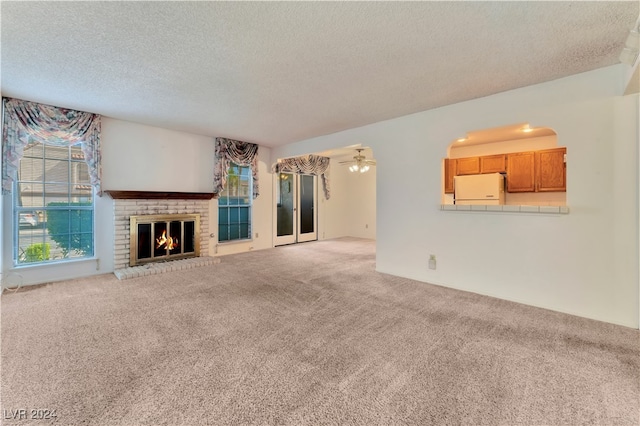 unfurnished living room with a textured ceiling, a brick fireplace, ceiling fan, and carpet floors