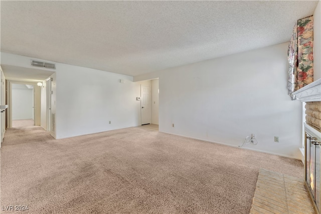 unfurnished living room featuring a textured ceiling, light carpet, and a brick fireplace