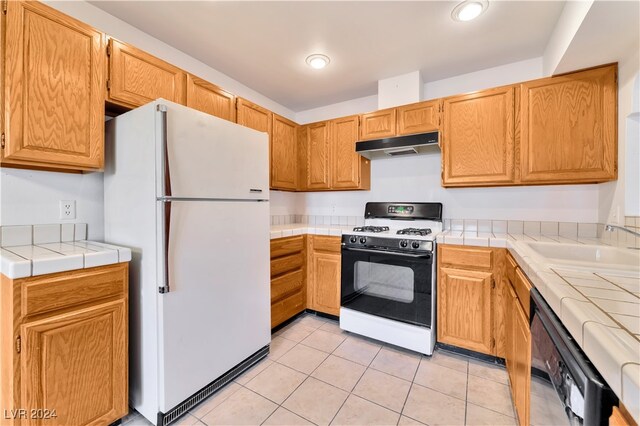 kitchen featuring tile counters, sink, light tile patterned floors, and white appliances