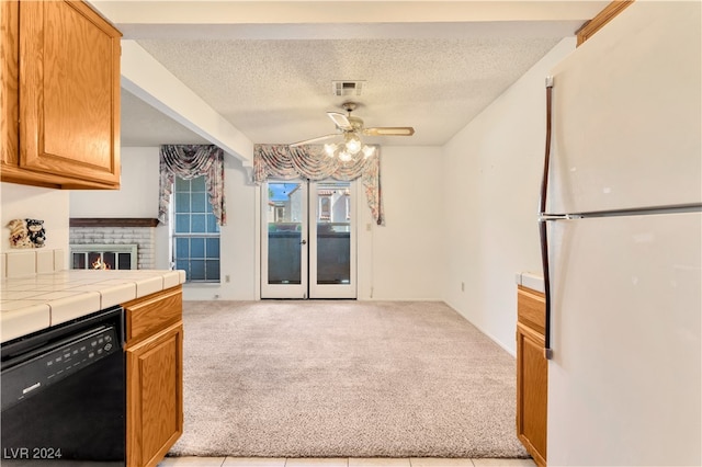 kitchen featuring dishwasher, tile countertops, a brick fireplace, ceiling fan, and white refrigerator