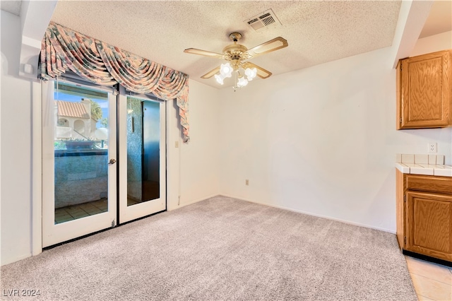 unfurnished dining area featuring ceiling fan, light carpet, and a textured ceiling