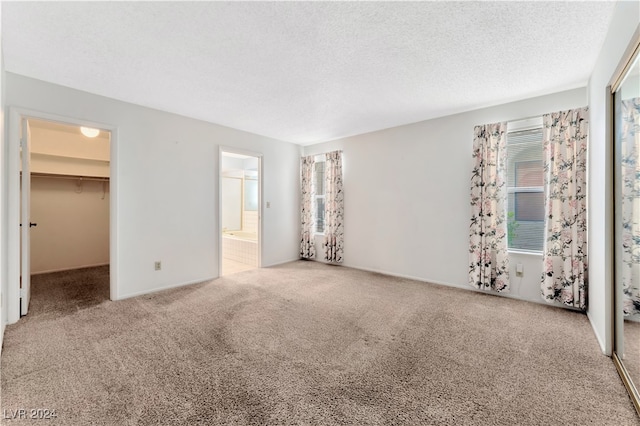 interior space with ensuite bath, a walk in closet, a closet, carpet floors, and a textured ceiling