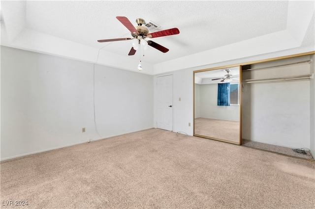 unfurnished bedroom with a textured ceiling, a raised ceiling, a closet, light colored carpet, and ceiling fan