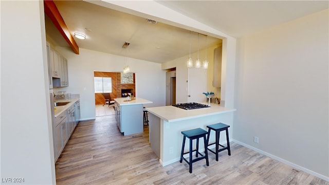 kitchen with light wood-type flooring, stainless steel gas cooktop, a kitchen breakfast bar, kitchen peninsula, and pendant lighting