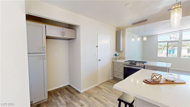 kitchen featuring white cabinets, hanging light fixtures, light hardwood / wood-style floors, and stainless steel gas range oven