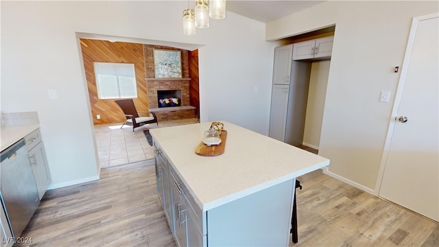 kitchen with dishwasher, pendant lighting, a brick fireplace, and light wood-type flooring