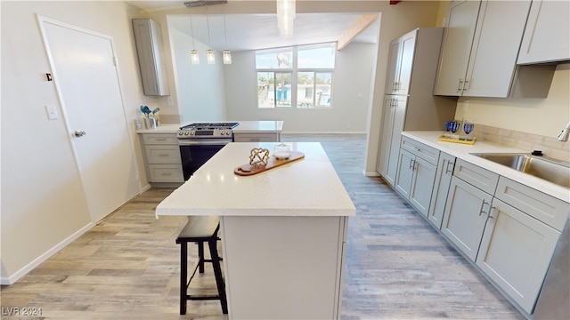 kitchen featuring gas range, pendant lighting, light hardwood / wood-style floors, a center island, and sink