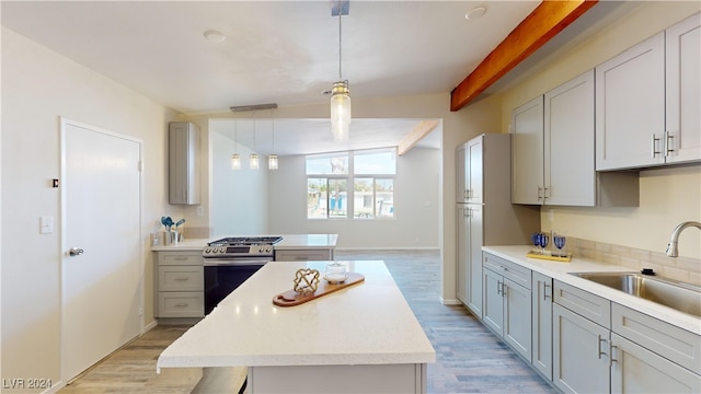 kitchen featuring sink, gray cabinets, stainless steel gas range, pendant lighting, and a kitchen island