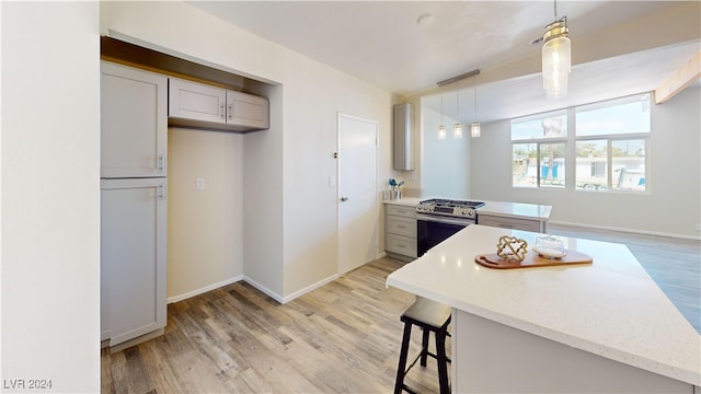 kitchen featuring light hardwood / wood-style flooring, decorative light fixtures, light stone counters, kitchen peninsula, and gas range