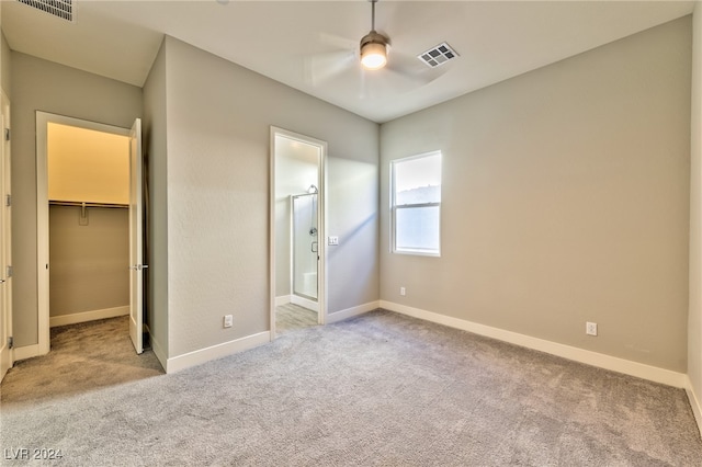 unfurnished bedroom featuring light colored carpet, ceiling fan, a closet, and a walk in closet