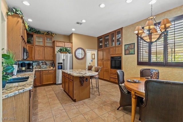 kitchen with a chandelier, black appliances, a kitchen island, light stone countertops, and a breakfast bar area