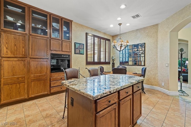 kitchen with hanging light fixtures, a center island, oven, light stone countertops, and a breakfast bar area