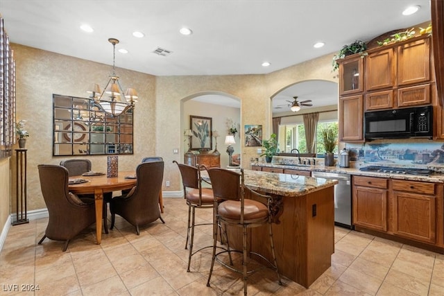 kitchen featuring decorative light fixtures, ceiling fan with notable chandelier, light stone counters, stainless steel appliances, and a kitchen island