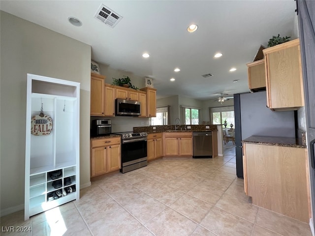 kitchen featuring dark stone countertops, light tile patterned floors, appliances with stainless steel finishes, sink, and ceiling fan