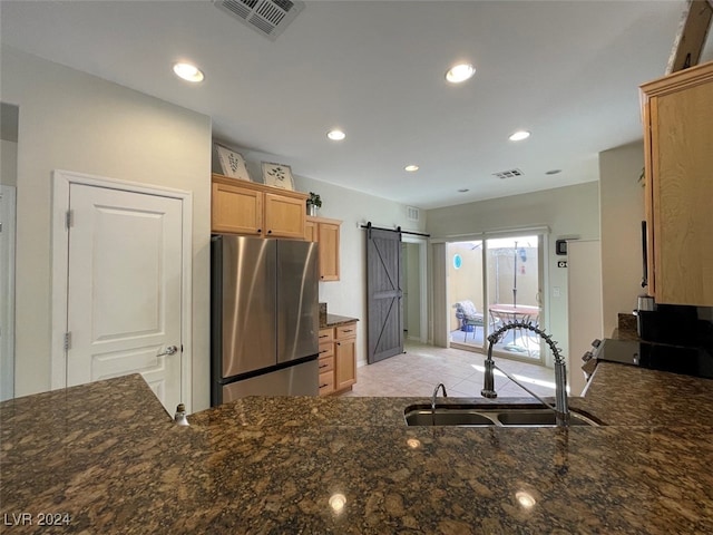 kitchen featuring kitchen peninsula, stainless steel refrigerator, sink, a barn door, and dark stone countertops