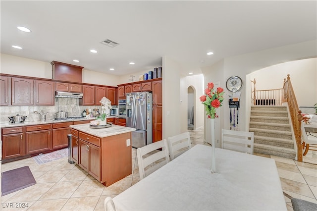 kitchen with a kitchen island, stainless steel appliances, light tile patterned floors, and decorative backsplash